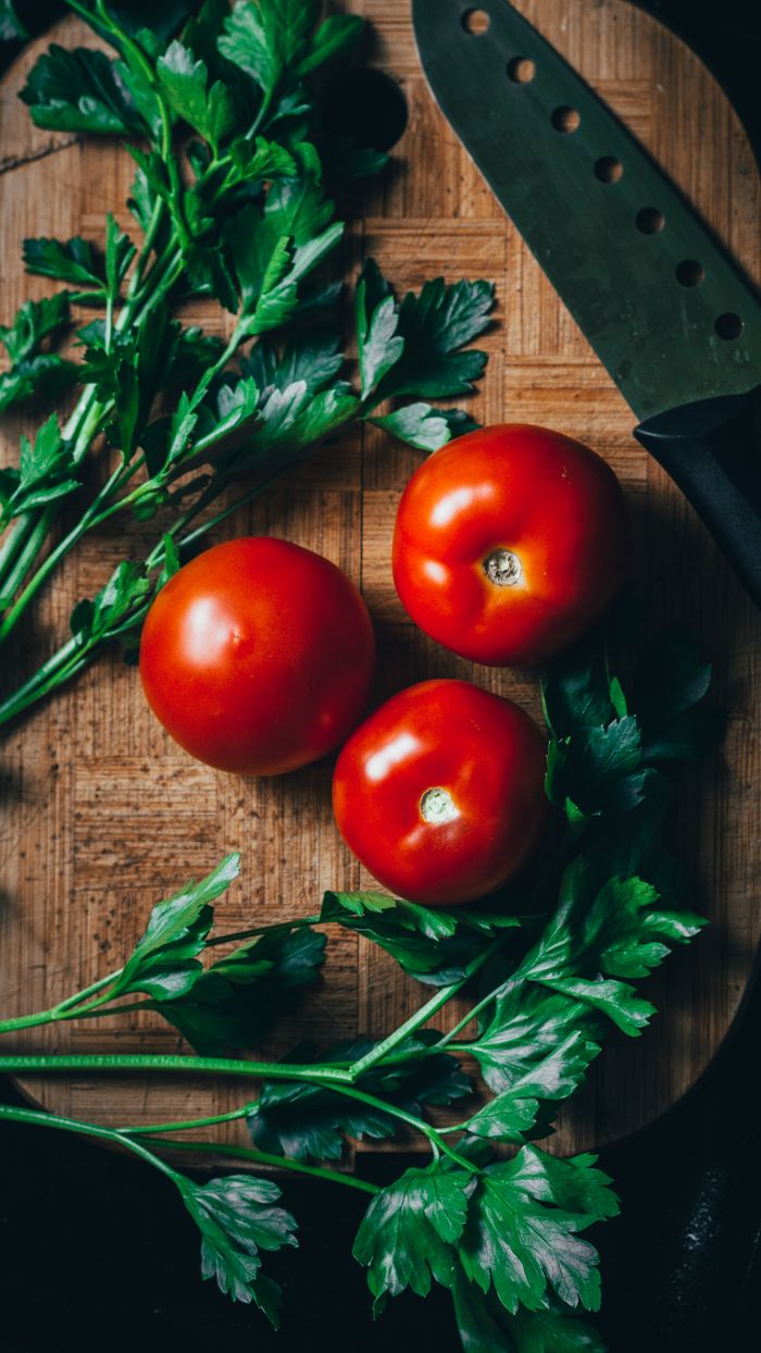 A vibrant composition of tomatoes and herbs on a wooden cutting board, ideal for culinary themes.