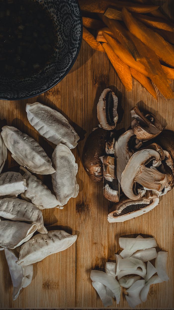Rustic arrangement of dumplings, mushrooms, and vegetables on a wooden board for cooking inspiration.