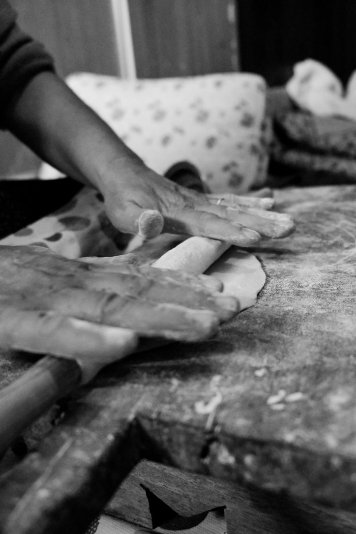 Monochrome image of hands using a rolling pin to flatten dough on a rustic surface.