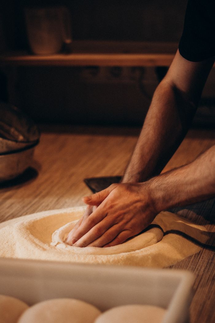 A baker's hands kneading dough in a cozy, dimly lit artisan bakery setting.