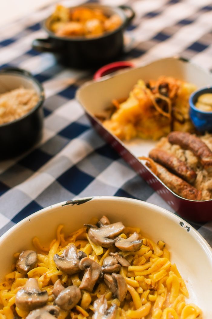 A variety of German dishes including creamy mushroom pasta on a checkered tablecloth.