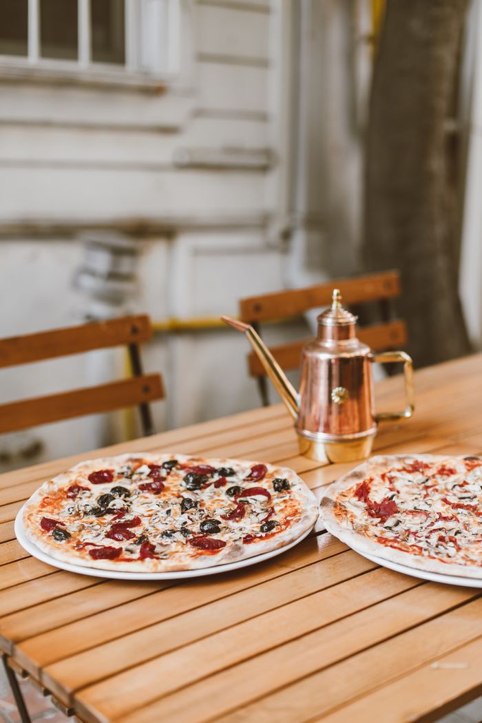 Two mouth-watering pizzas and a copper kettle on a wooden table, perfect for outdoor dining.